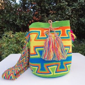 May include: A colorful crocheted bag with a geometric pattern in shades of green, blue, orange, and yellow. The bag has a long strap and two colorful tassels.
