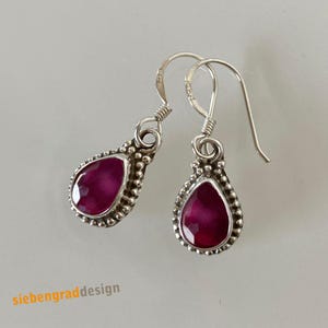 Könnte beinhalten: Ein Paar silberne Ohrhänger mit tropfenförmigen rosafarbenen Edelsteinen. Die Ohrringe haben einen perlenbesetzten Rand um die Edelsteine.