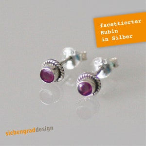 Könnte beinhalten: Ein Paar silberne Ohrstecker mit facettierten Rubin-Edelsteinen. Die Ohrringe sind in einer silbernen Zarge mit einem seilartigen Rand gefasst. Der Text "facettiert Rubi in Silber" ist im Bild sichtbar.