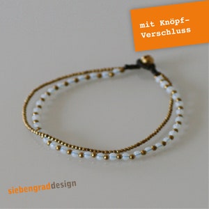 Könnte beinhalten: Ein doppelreihiges Armband mit weißen Perlen und goldenen Akzenten. Das Armband hat einen Knopfverschluss und der Text "mit Knopf-Verschluss" ist im Bild sichtbar.