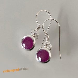 Könnte beinhalten: Silberne Ohrhänger mit runden, tiefrosa Edelsteinen. Die Edelsteine sind in einer Zargenfassung gefasst. Die Ohrringe haben ein schlichtes, elegantes Design. Der Text "siebengraddesign" befindet sich unten links.