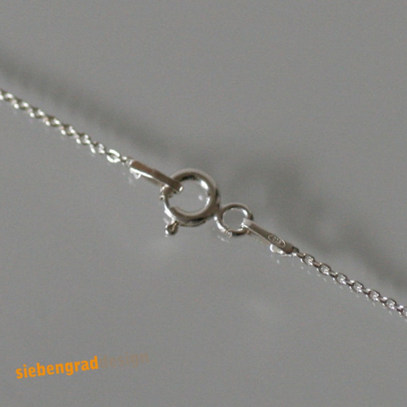 May include: Close-up of a silver chain necklace clasp with a lobster claw closure. The chain is a delicate, twisted design.