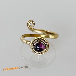 Könnte beinhalten: Ein goldener Ring mit einem violetten Stein, der in einer dekorativen Fassung sitzt. Der Ring ist so konzipiert, dass er sich um den Finger wickelt.