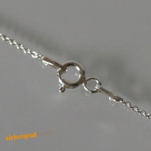 May include: Close-up of a silver chain necklace clasp. The clasp is a lobster claw style with a small jump ring.