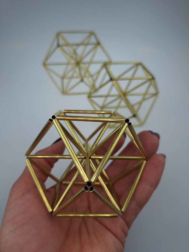 May include: Three geometric sculptures constructed from thin, hollow gold-toned metal rods. Each sculpture features a complex, multi-faceted polyhedral frame with open vertices. The structures are arranged with one in the foreground and two behind.