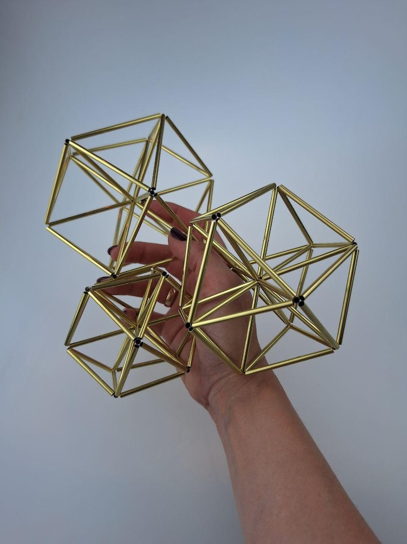 May include: Three geometric sculptures constructed from thin, metallic gold-toned rods connected at black joints. The structures feature interconnected triangular and square frames, forming complex polyhedral shapes with an open, airy design.