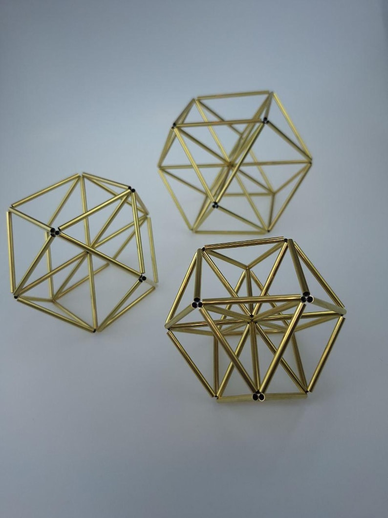 May include: Three geometric sculptures constructed from thin, metallic gold-colored rods. Each object features a complex, multi-faceted polyhedral frame with open spaces between the connected bars, creating a three-dimensional wireframe structure.