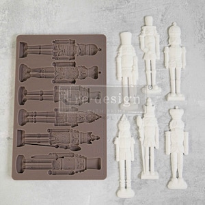 May include: A brown silicone mold with six different nutcracker designs.  Next to the mold are six white nutcracker figurines.