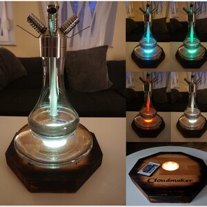 Könnte beinhalten: Eine moderne Shisha mit einem transparenten Glaskörper, Edelstahlakzenten und einem Holzsockel. Die Shisha verfügt über ein mehrfarbiges LED-Lichtsystem, und die Basis ist mit dem Wort "Cloudmaker" graviert.