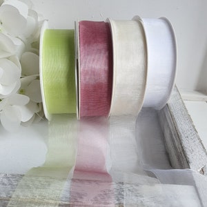 Könnte beinhalten: Vier Spulen mit transparentem Band in Grün, Burgunderrot, Creme und Weiß. Das Band wird auf einer weißen Spule präsentiert und ist teilweise abgerollt, wodurch die durchscheinende Textur sichtbar wird. Ideal für Bastelarbeiten und Geschenkverpackungen.