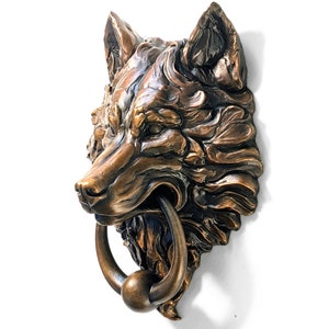 May include: A bronze wolf head door knocker with a detailed design and a round, metal ring.
