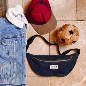 May include: A dark blue denim fanny pack with a gold zipper and a white label that says "MAISON BOHOISH".