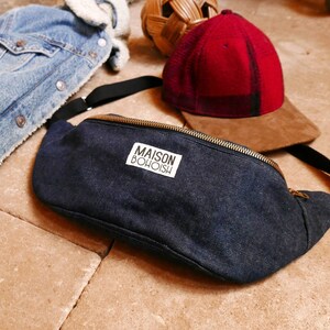 May include: A dark blue denim fanny pack with a gold zipper and a white label that reads "MAISON BOHOISH".