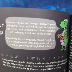 May include: A green dinosaur character wearing red oven mitts holds a baking sheet with chocolate chip cookies. The text reads "Hi there! I'm Jake and I've got loads of top tips to help you bake. You will see me throughout this recipe book with helpful information that will make you a rock star in the kitchen."  The text also reads "Every recipe has a guide to show you how easy or difficult it might be, some may take a few minutes or only have a few ingredients. Others require time, have more ingredients or more complex steps to follow."
