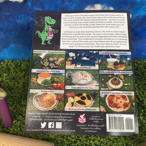 May include: The back cover of a cookbook titled "SciRecipes" features a green dinosaur holding a baking sheet. The cover is divided into nine squares, each showcasing a different recipe with a science-themed name. The book is printed by Totally Roarsome Books.