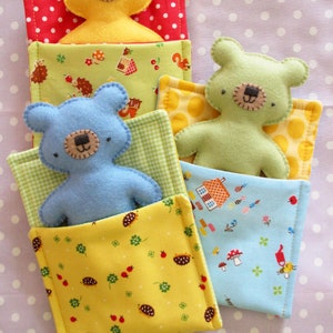 May include: Three plush teddy bears in different colors, each sleeping in a colorful fabric bed. The beds are stacked on top of each other, with the yellow bear on top, the green bear in the middle, and the blue bear on the bottom.