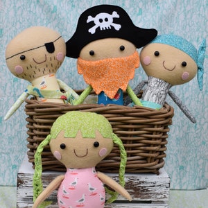 May include: Handmade felt dolls, including a pirate, a mermaid, and two other characters in a woven basket. The pirate doll wears a black hat with a skull and crossbones. The mermaid doll has a pink body with a seagull pattern.