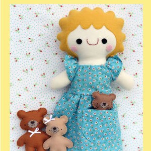 May include: A handmade doll with blonde hair and a blue dress with white polka dots. The doll is holding a small brown teddy bear in her pocket. Two other brown teddy bears are sitting in front of the doll. The image is captioned "Goldilocks and the Three Bears".