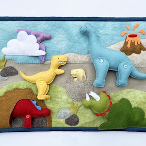 May include: A felt play mat with a blue border features a variety of dinosaurs, including a yellow T-Rex, a blue long-necked dinosaur, a purple pterodactyl, a green triceratops, and a brown volcano.