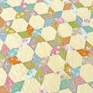 Peut inclure: Une courtepointe avec un motif de étoiles répétées faites de différents tissus floraux dans des tons de rose, bleu, vert et marron. Le tissu de fond est jaune clair.