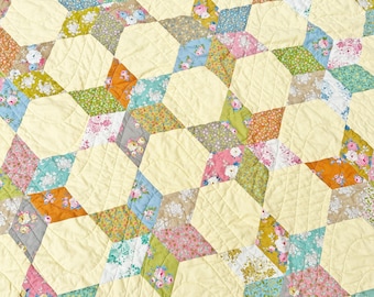 May include: A quilt with a pattern of repeating stars made from different floral fabrics in shades of pink, blue, green, and brown. The background fabric is a light yellow.