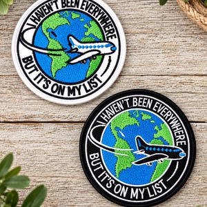 May include: Two circular embroidered patches featuring a globe with green continents and blue oceans. A white airplane with a flight path arc is centered on the globe. The text "HAVEN'T BEEN EVERYWHERE BUT IT'S ON MY LIST" circles the design.