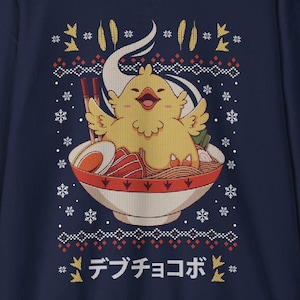 Peut inclure: Sweat-shirt bleu marine avec un dessin de poussin de dessin animé dans un bol de ramen. Le poussin est jaune et le bol contient des nouilles, un œuf et d'autres ingrédients de ramen. Le design comprend des flocons de neige et le texte japonais "Debu Chocobo".