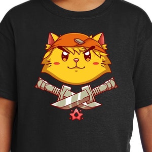 Könnte beinhalten: Schwarzes T-Shirt mit einem Cartoon-Bild eines gelben Katers, der ein rotes Bandana trägt und zwei Schwerter hält. Die Katze hat einen ernsten Ausdruck und ist von einem roten Stern umgeben.