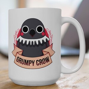 May include: White ceramic mug with a cartoon illustration of a grumpy crow with red cheeks and a ruffled collar. The crow is wearing a banner that says "Grumpy Crow".