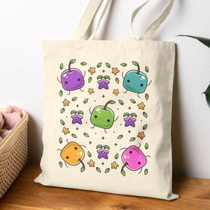 May include: A cream-colored tote bag featuring a repeating pattern of cartoon fruit characters in various colors, including purple, green, blue, orange, and pink. The design includes stars and leaves. The bag has a simple, minimalist design.