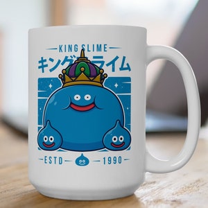 Può includere: Una tazza in ceramica bianca con un'illustrazione blu e verde di un mostro di slime dei cartoni animati che indossa una corona. Il testo "KING SLIME" e "キング スライム" è stampato sulla tazza. Il testo "ESTD 1990" è anche stampato sulla tazza.