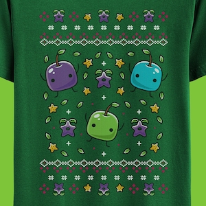 Könnte beinhalten: Grünes T-Shirt mit einem Weihnachtspullover-Design mit lila, blauen und grünen Comicfiguren mit Sternen und Blättern.