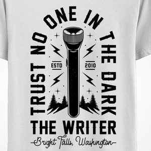 May include: White t-shirt featuring a black graphic of a flashlight with the text "ONE IN THE DARK" and "TRUST NO ONE". Below the flashlight is "THE WRITER" and "Bright Falls, Washington".