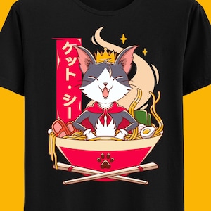 Op de afbeelding: Een zwart T-shirt met een cartoonkat die een kroon en een rode cape draagt, zittend in een kom ramennoedels. De Japanse tekst aan de zijkant zegt "クッド・ラリー".