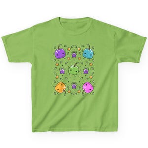 May include: A green t-shirt with a pattern of colorful cartoon apples with faces. The apples are arranged in a grid pattern with green leaves and yellow stars.