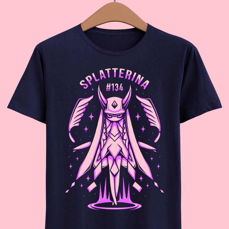 May include: A navy blue t-shirt with a pink graphic of a character with wings and horns. The text "splatterina #134" is above the character.