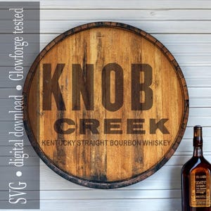 May include: A round wooden sign with the words "KNOB CREEK" in large, dark letters. Below, it reads "KENTUCKY STRAIGHT BOURBON WHISKEY." The sign is made from a repurposed barrel head. A bottle of whiskey is to the right.