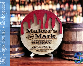 May include: A wooden round sign with a red dripping paint design. The sign says "Maker's Mark Kentucky Straight Bourbon Whisky Handmade" and includes the distillery information. The sign is on a small wooden stand and is next to two wooden barrels.