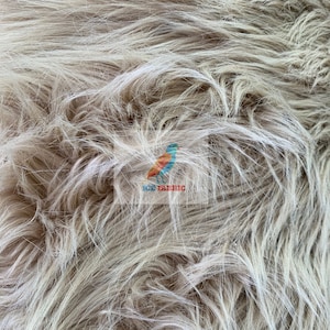 May include: Close-up of a beige faux fur fabric with long, shaggy fibers. The fabric has a soft, textured appearance with varying shades of beige and white. The image includes the text "ICE FABRIC" with a colorful bird logo.