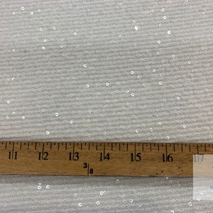 May include: White fabric with small, iridescent sequins. A ruler is placed on the fabric, showing measurements from 10 to 18 inches.