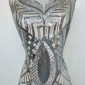 May include: Silver and gold sequined fabric with a geometric design. The fabric is on a white mannequin.