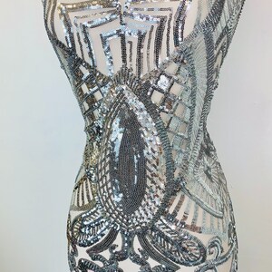 May include: Silver sequined fabric with a geometric pattern. The fabric is sheer and has a delicate, intricate design.