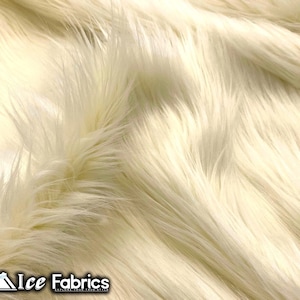 Puede incluir: Primer plano de una tela de piel sintética de color crema. La tela tiene fibras largas, suaves y esponjosas, creando una superficie texturizada. El logotipo de Ice Fabrics es visible en la esquina inferior izquierda.