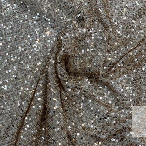 May include: A close-up of a gold and silver sequined fabric. The sequins are small and evenly spaced, creating a shimmering effect.