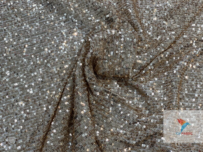 May include: A close-up of a gold and silver sequined fabric. The sequins are small and evenly spaced, creating a shimmering effect.