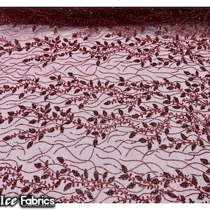 Puede incluir: Tela de encaje de color rojo burdeos con un delicado patr&oacute;n floral. La tela tiene un brillo sutil y es perfecta para crear prendas o accesorios elegantes.