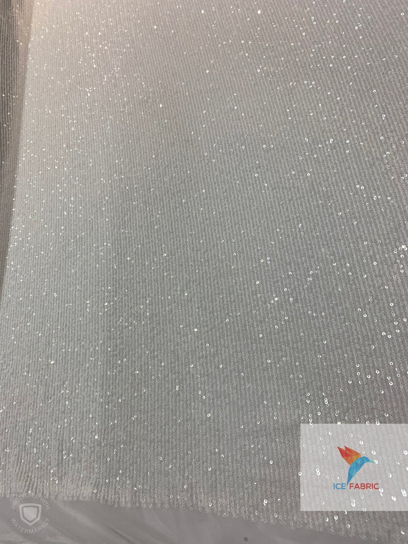 May include: White fabric with a subtle shimmer from small, evenly spaced sequins. The fabric has a slight texture, creating a ribbed effect. The fabric is shown against a white background.