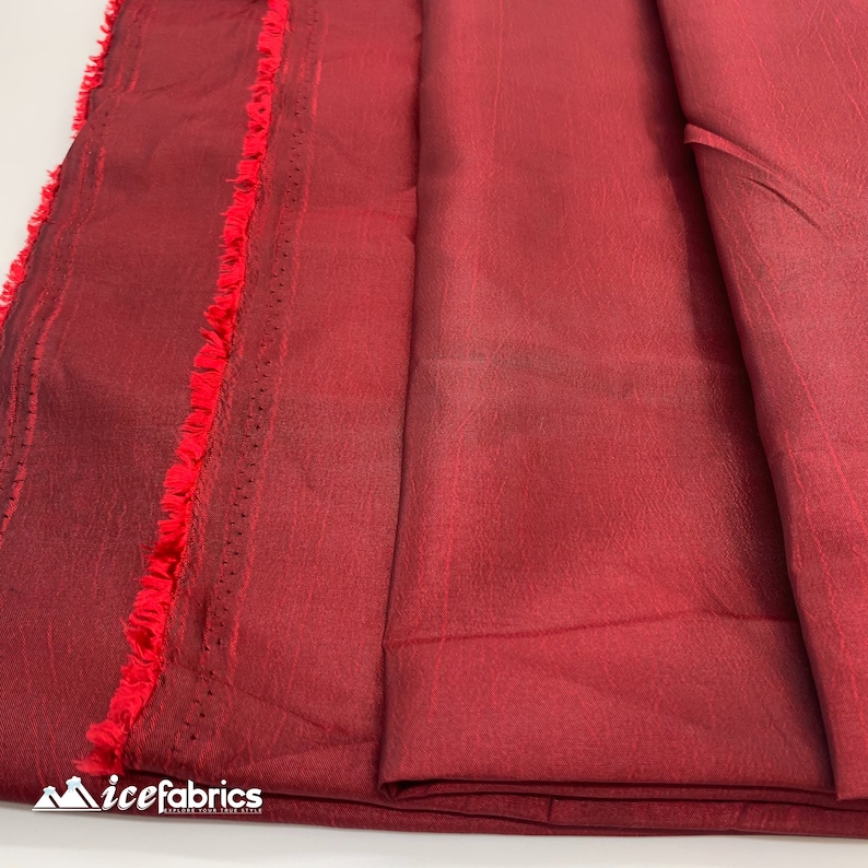 May include: Close-up of a deep red fabric with a subtle sheen. The fabric is folded and has a fringed edge.