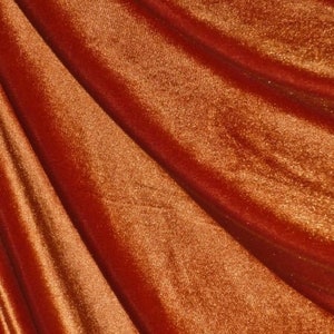 May include: Close-up of a rich, rust-colored velvet fabric with a soft, plush texture. The fabric has a subtle sheen and a slightly textured surface.