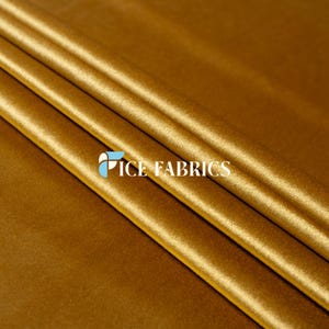 Op de afbeelding: Close-up van een goudgeel fluwelen stof met zichtbare plooien. De stof heeft een zachte, glanzende uitstraling. De tekst "ICE FABRICS" is in het wit op de stof gedrukt.